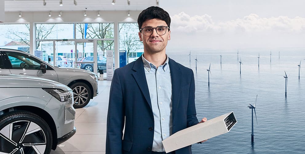 Mann hält Aktenordner. Im Hintergrund ist ein Autohaus und ein Offshore Windpark zu sehen.